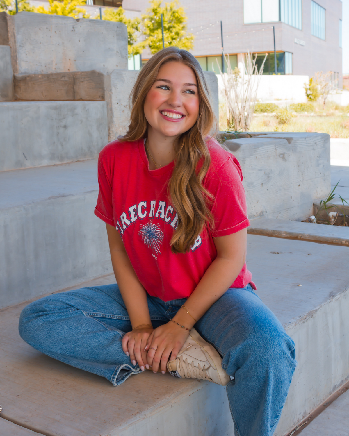 Firecracker written in white with a red white and blue firecracker burst art work on a red crew neck tee with small side slit 