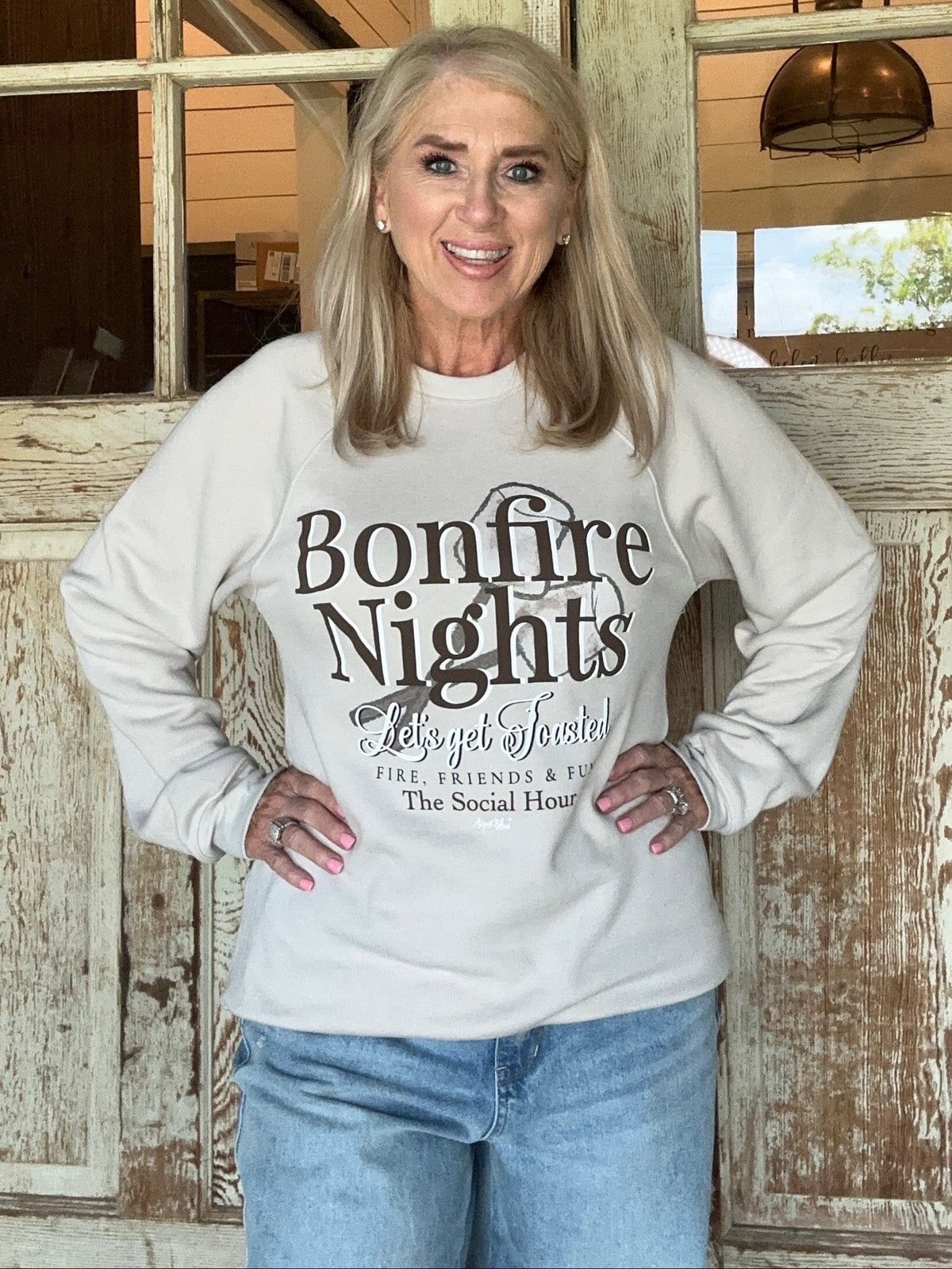 Woman wearing a sweatshirt with 'Bonfire Nights' text in a rustic indoor setting.
