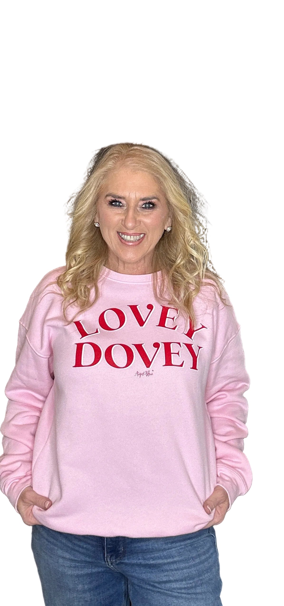 Woman wearing a pink sweatshirt with 'LOVEY DOVEY' text in red, standing against a wooden door background.