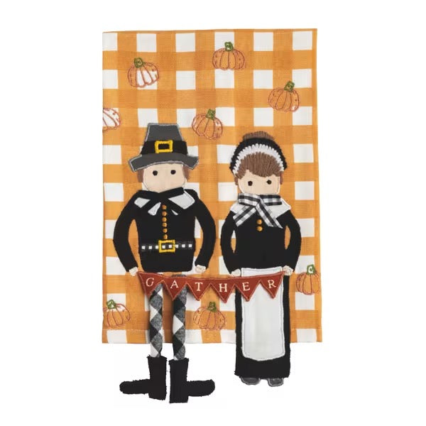 A square kitchen towel with a Thanksgiving-themed design, featuring a man and woman in colonial-style clothing standing in front of an orange and white gingham background with pumpkins. The word 'GATHER' is displayed on a banner held by the figures.