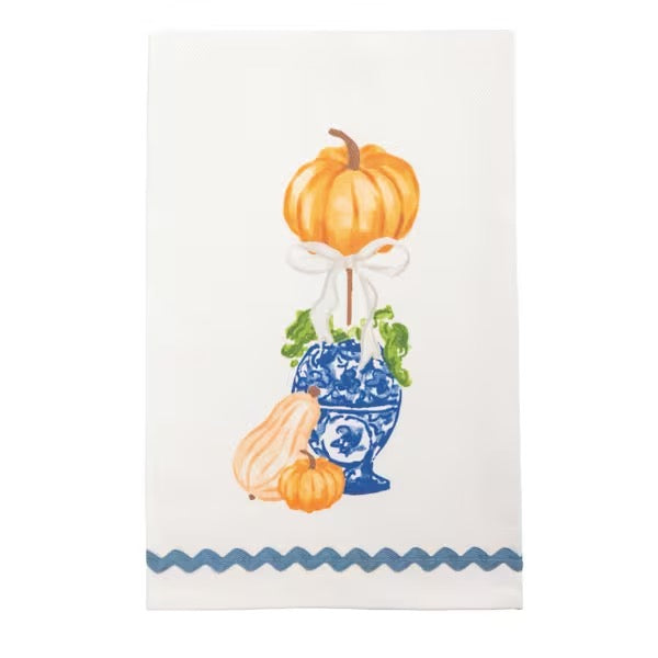 An off-white kitchen tea towel featuring a watercolor-style autumn harvest illustration with pumpkins, a blue-and-white patterned vase, green leaves, and a blue wavy stripe along the bottom edge.