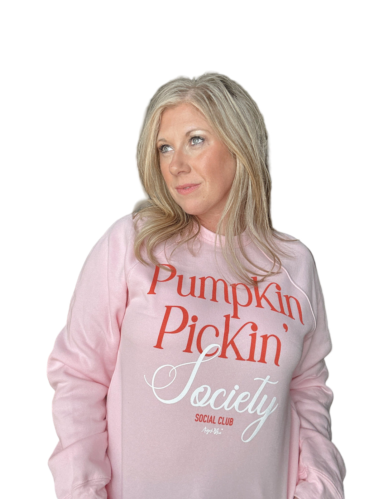 Woman wearing a pink sweatshirt with &#39;Pumpkin Pickin Society&#39; text in an indoor setting.
