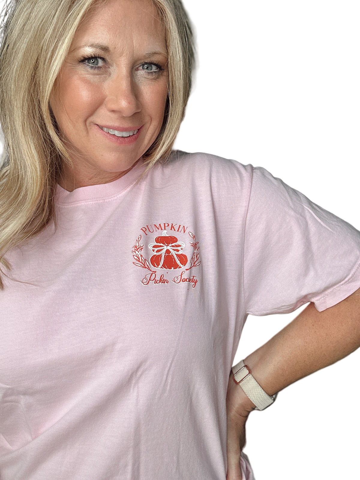 Woman wearing a pink t-shirt with a pumpkin logo and text, standing indoors.