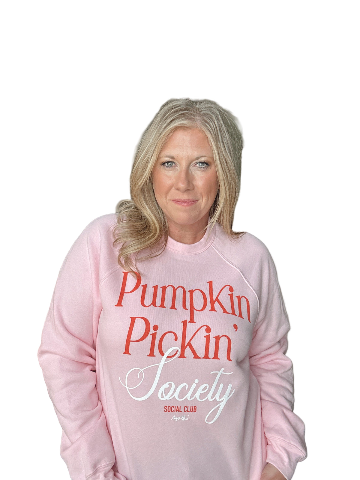 Woman wearing a pink sweatshirt with &#39;Pumpkin Pickin&#39; Society&#39; text in a casual setting.