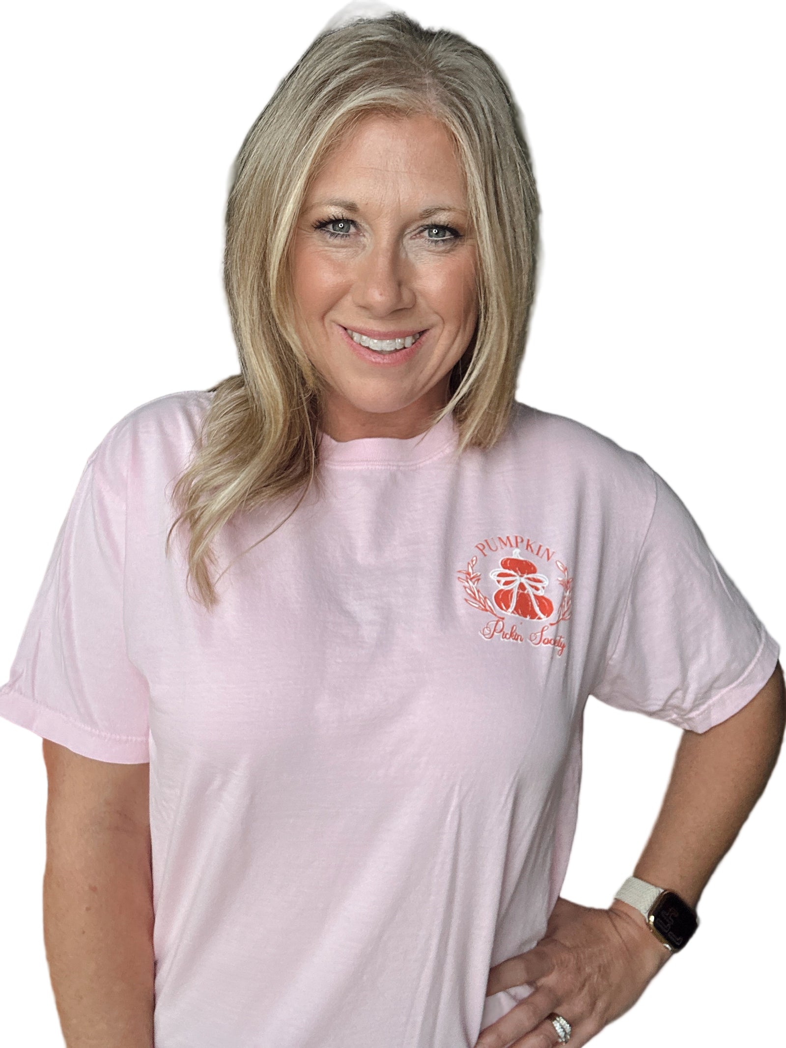 Woman wearing a light pink t-shirt with a pumpkin logo, standing indoors.