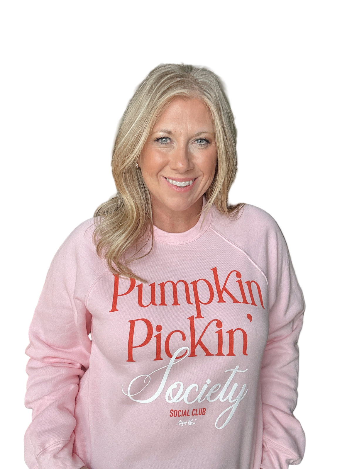Woman wearing a pink sweatshirt with &#39;Pumpkin Pickin&#39; Society&#39; text in a casual setting.