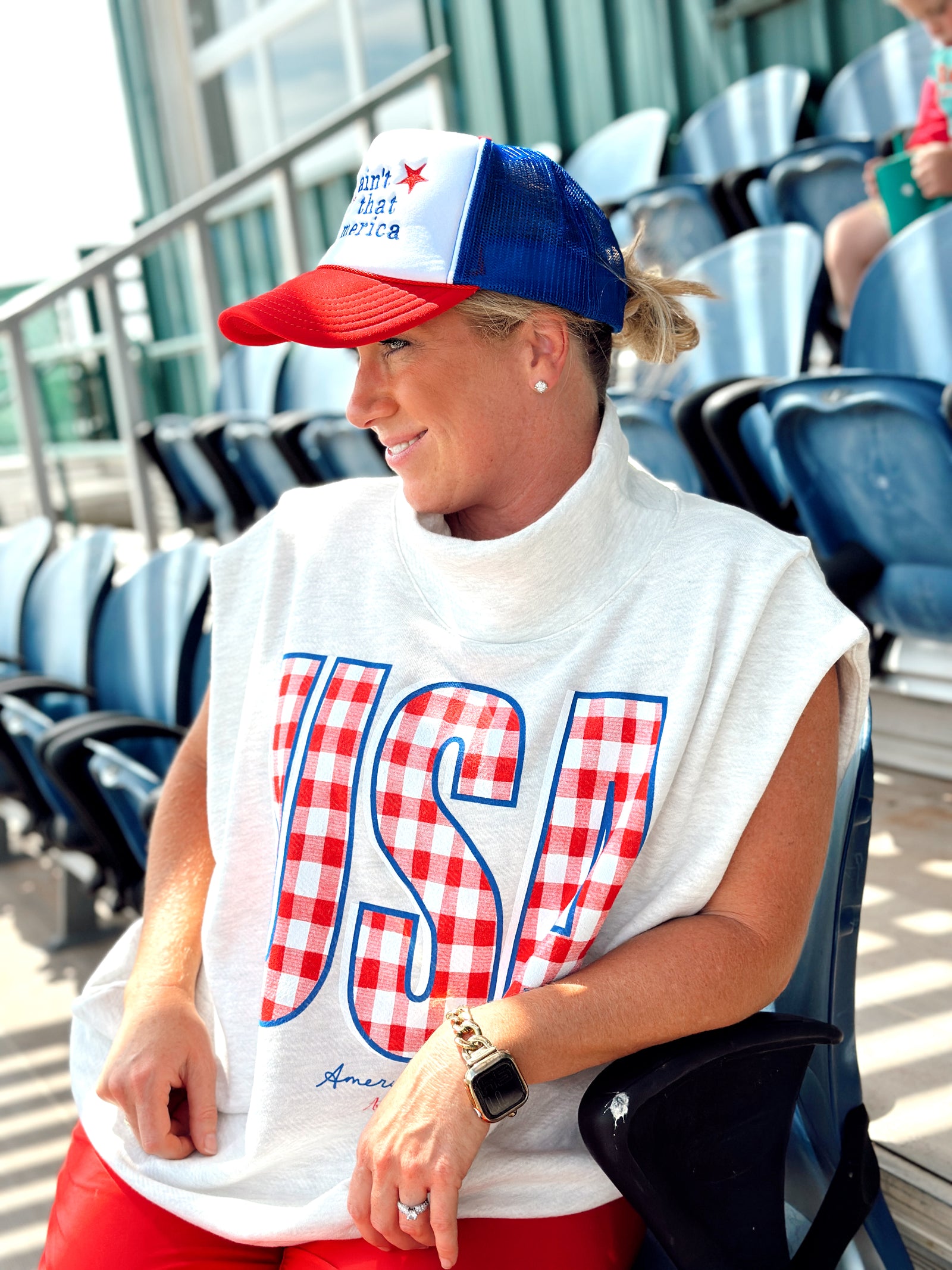 Person wearing a light grey Americana 250 sleeveless shirt with 'USA' printed in red and blue, sitting in a stadium.