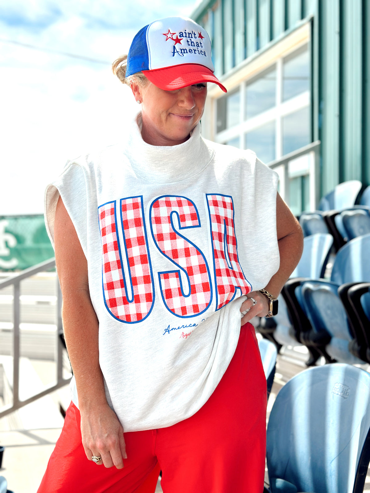 Person wearing a white sleeveless shirt with 'USA' in red and blue, red pants, and a red, white, and blue cap outdoors.