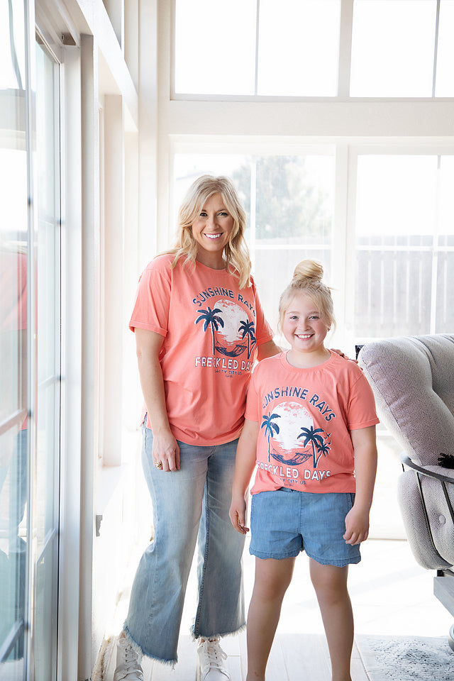 Sunshine rays and freckled days coral short sleeve tee- palm tree hammock and setting sun graphic shown on a mom and daughter 